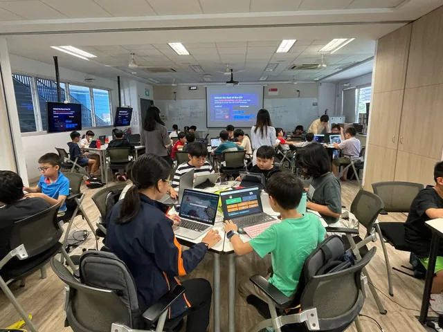 Teams of competitors working at laptops during a Capture-the-Flag cybersecurity competition in a classroom with a projection screen