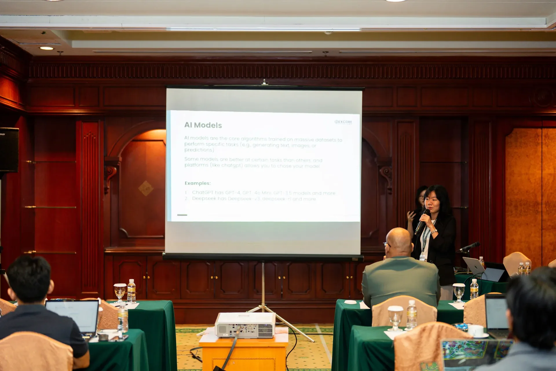 A presenter conducts a workshop on AI Models at CYSEC 2025 Brunei Conference, with attendees seated at tables in a wood-panelled conference room