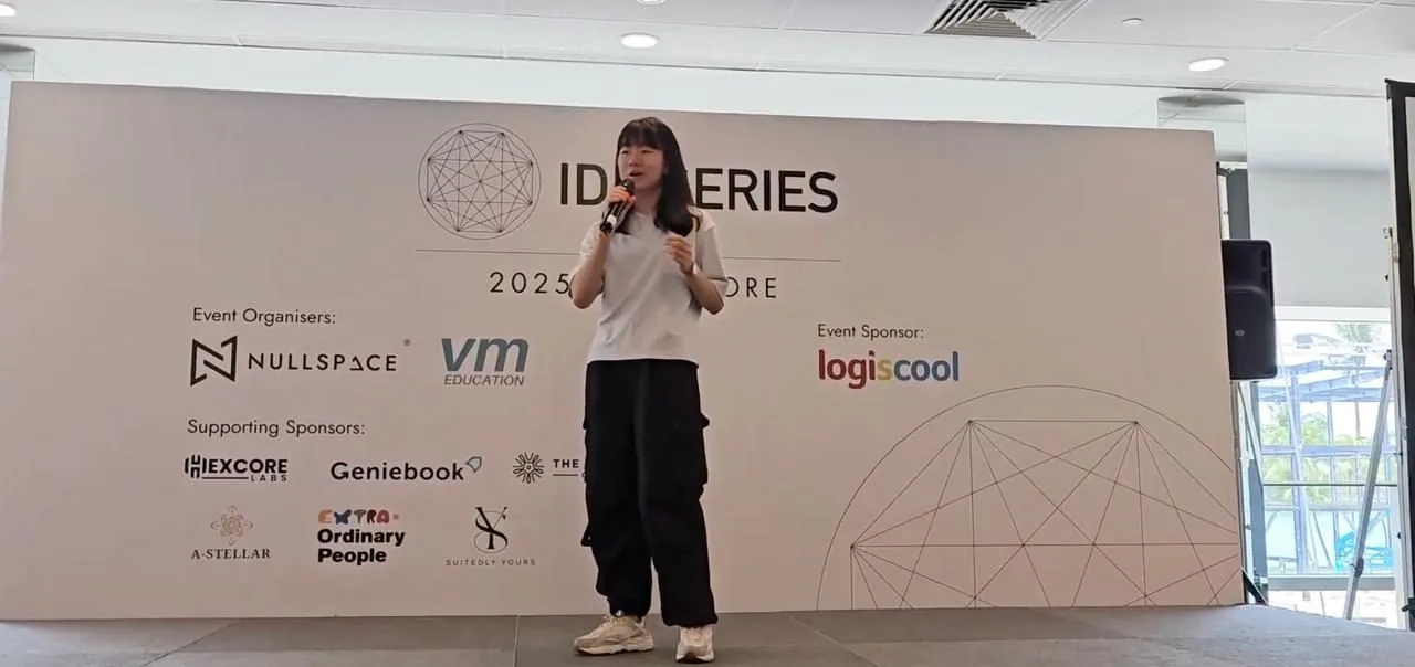 Woman speaking at IDE Series 2025 Singapore event, standing in front of branded backdrop with sponsor logos