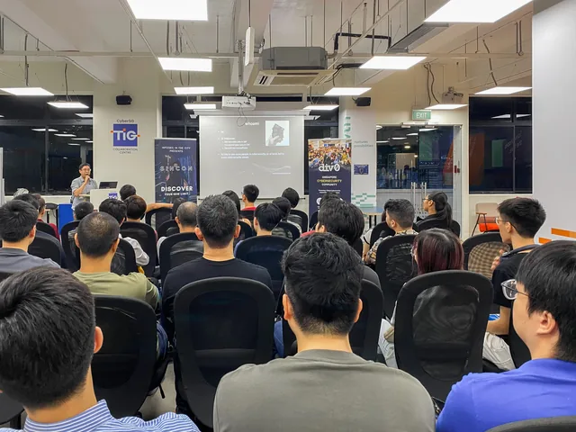 Cybersecurity enthusiasts seated in rows facing a projection screen during a Division 0 meetup demonstration on penetration testing and OSCP preparation