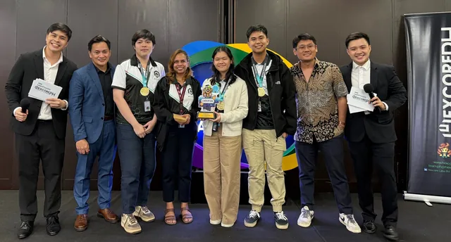 Nine people standing in a line at an indoor event, with two in the centre wearing medals, holding a trophy, and a colourful banner behind them
