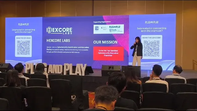 A presenter stands on stage at the Plug and Play APAC Summit 2024, delivering a pitch in front of a large screen displaying Hexcore Labs branding and mission in