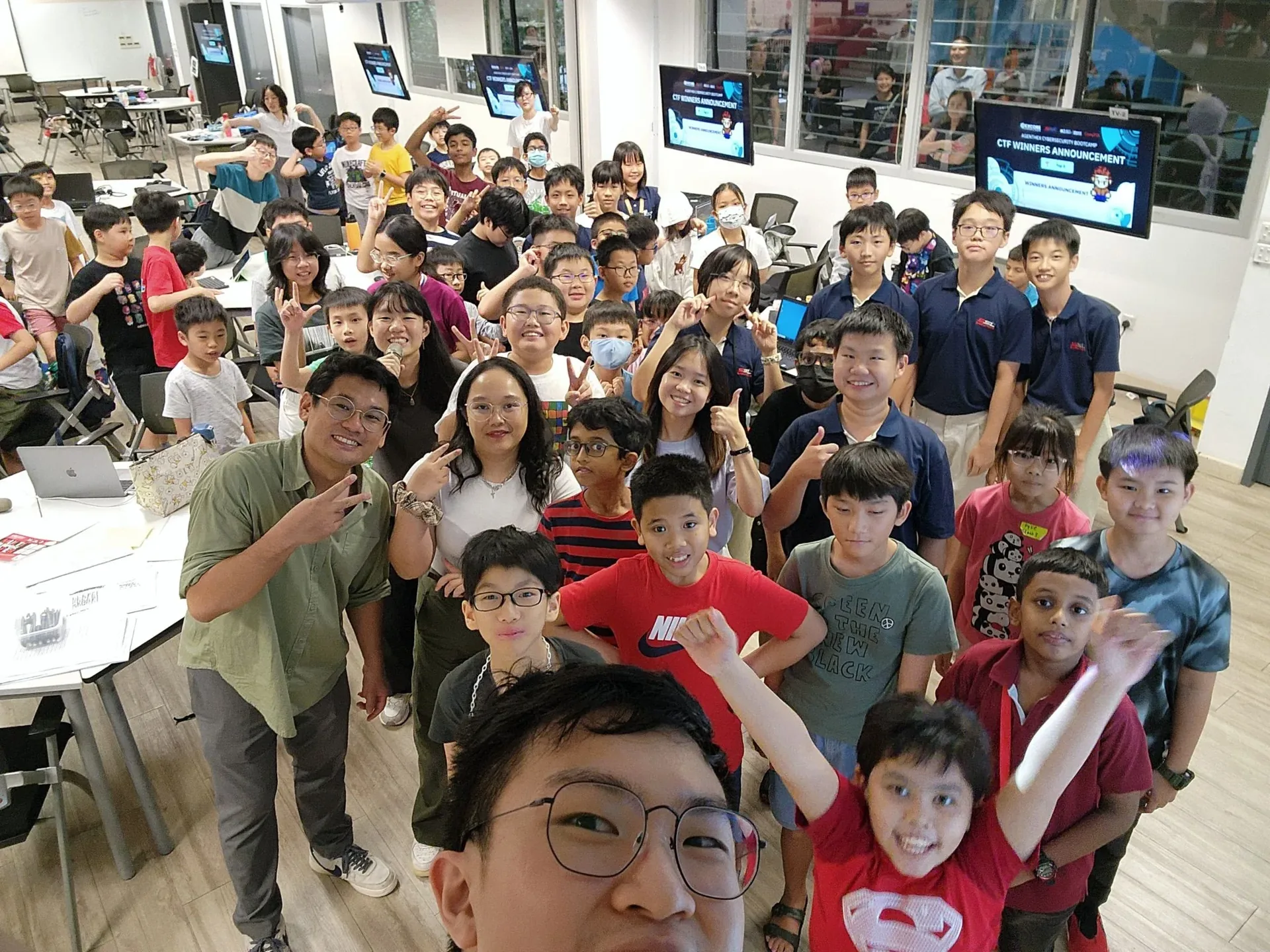 Large group of upper primary students gathered in a modern classroom during the AgentHex Cybersecurity Bootcamp, with screens visible in the background