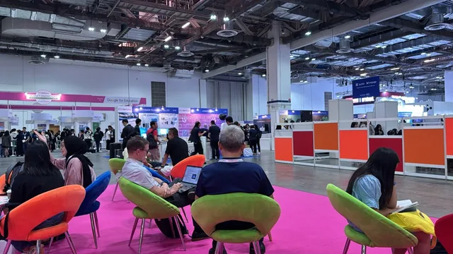 People seated on colourful chairs at SWITCH 2024 exhibition hall with booths and attendees in background
