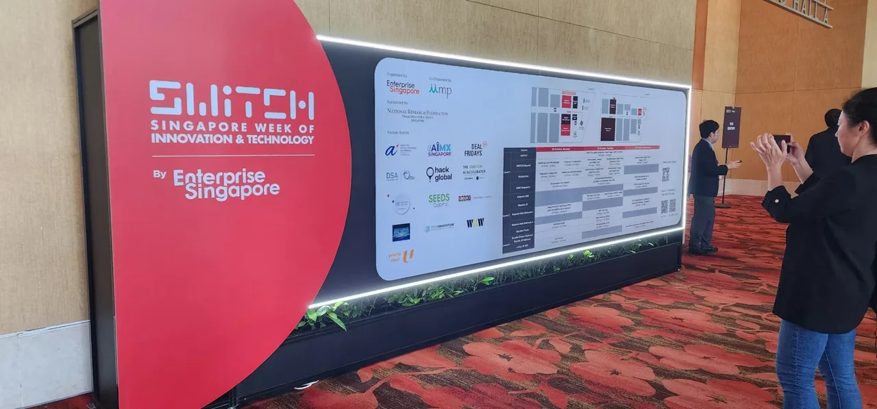 SWITCH 2024 exhibition booth with red signage and display panels, visitors viewing the CyberSG Talent, Innovation and Growth Centre showcase