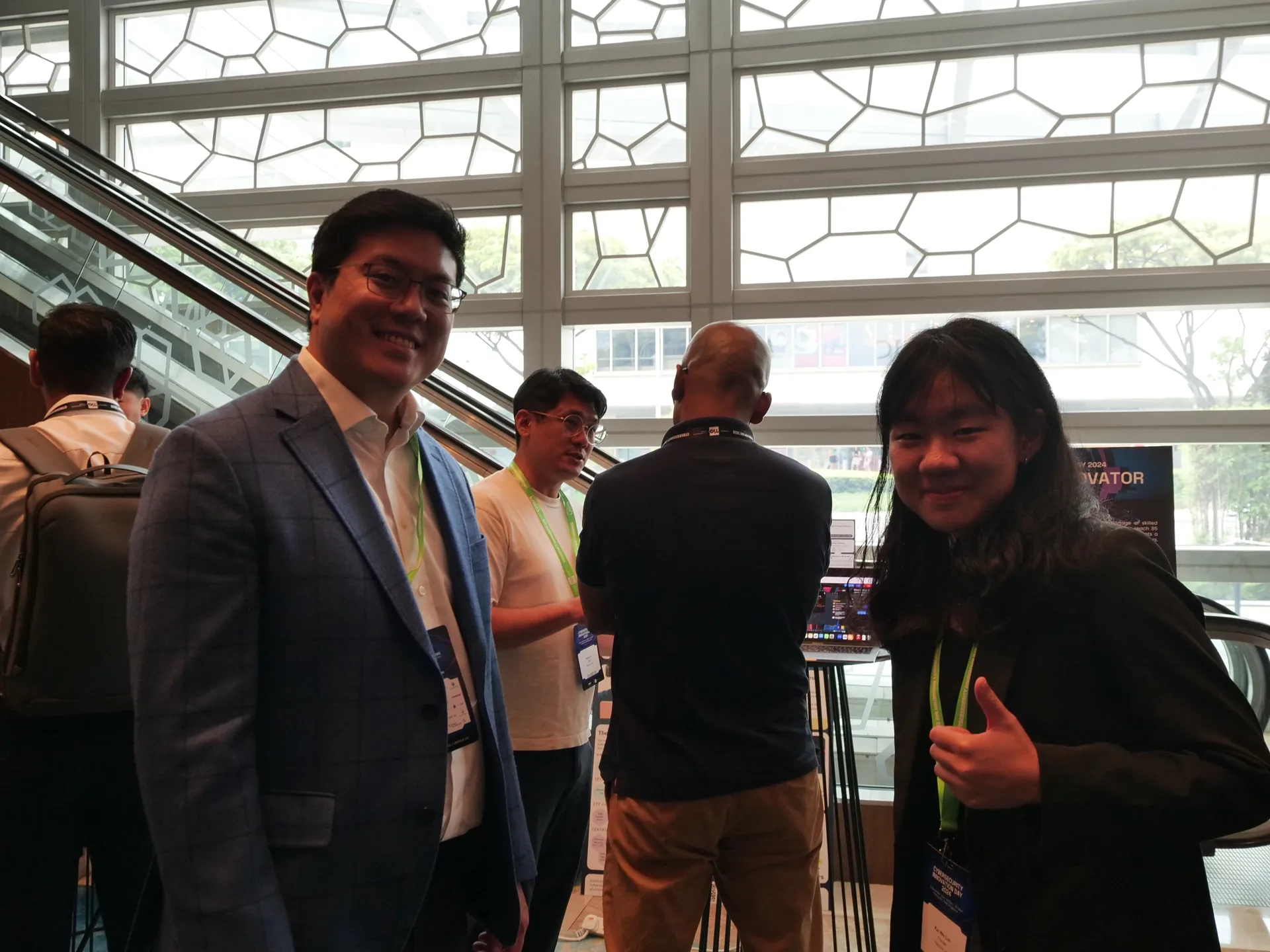 People at an exhibition booth inside a modern venue with geometric ceiling panels, during the Cybersecurity Innovation Day 2024