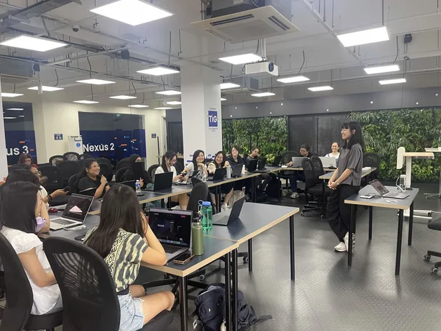 Women participants seated at desks with laptops during a cybersecurity workshop in a modern office space with green plant walls