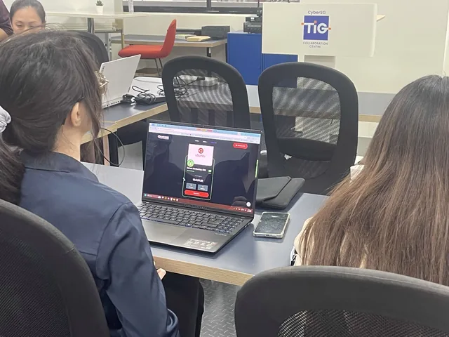 Women participants seated at a desk during a cybersecurity workshop, viewing a laptop screen in an office setting